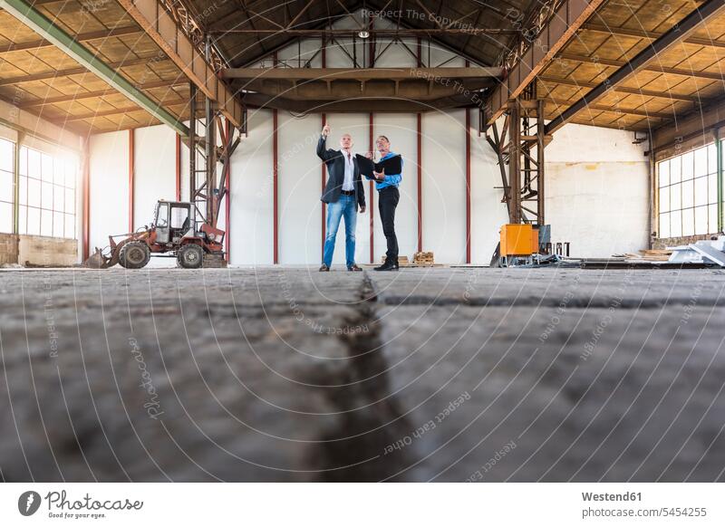 Two businessmen with documents talking in old industrial hall speaking man males Businessman Business man Businessmen Business men colleagues working At Work