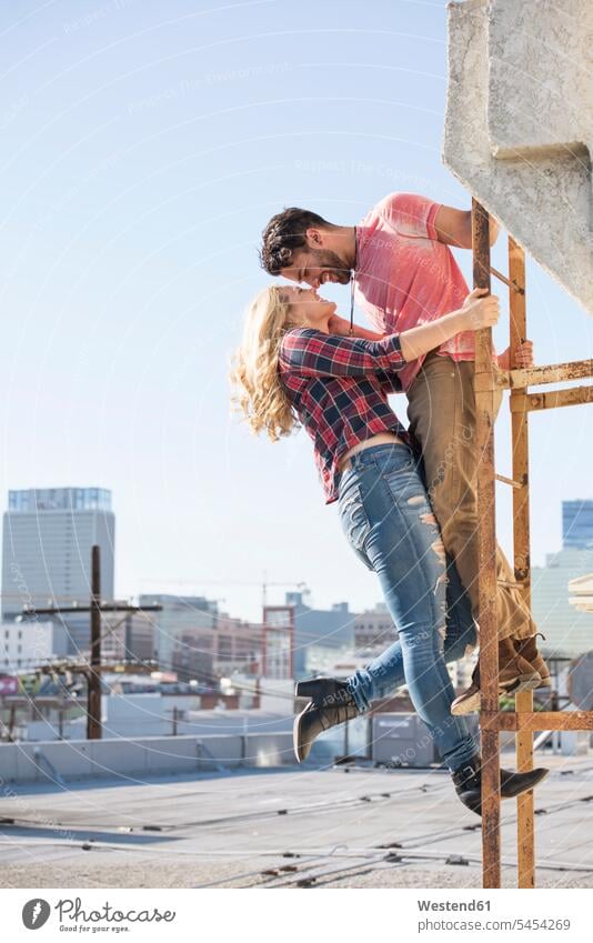 Young couple kissing on a fire escape on a roof in love happiness happy twosomes partnership couples kisses roof terrace deck rooftop standing ladder ladders