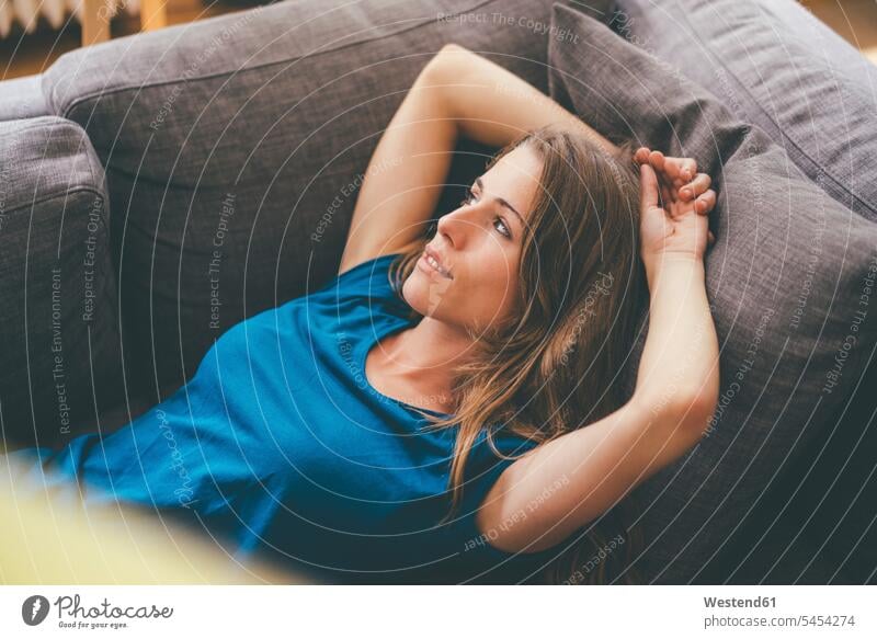 Relaxed young woman lying on couch at home laying down lie lying down smiling smile females women relaxed relaxation settee sofa sofas couches settees Adults