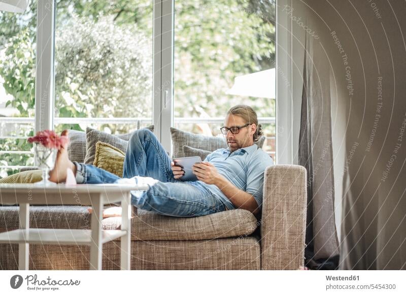 Man relaxing on couch using tablet settee sofa sofas couches settees relaxed relaxation man men males digitizer Tablet Computer Tablet PC Tablet Computers iPad