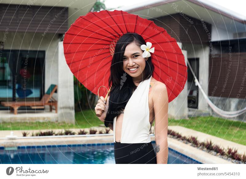 Portrait of smiling woman with flower in her hair holding a red tradtional umbrella at a swimming pool Brolly umbrellas portrait portraits pools swimming pools