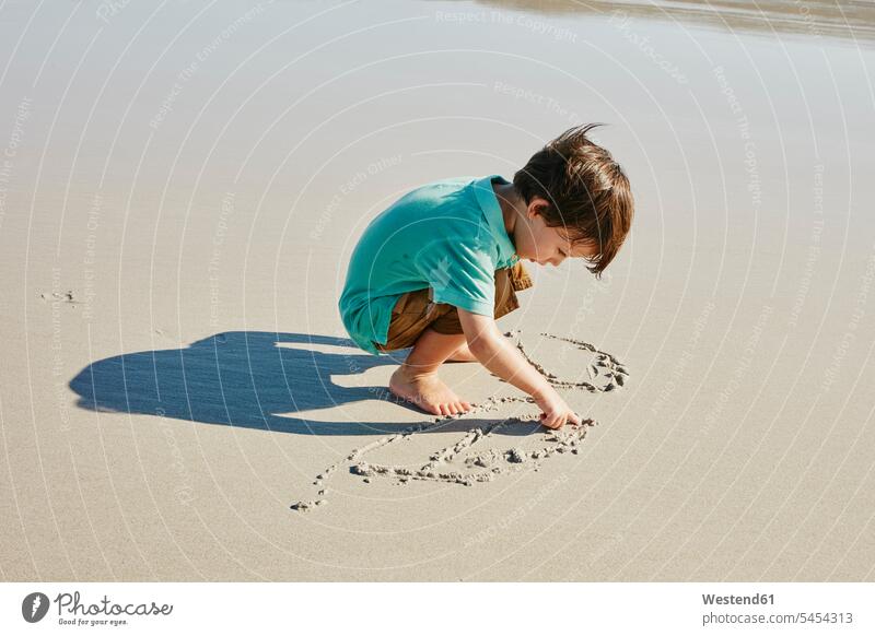 Little boy drawing in the sand on the beach boys males beaches scratching child children kid kids people persons human being humans human beings crouching