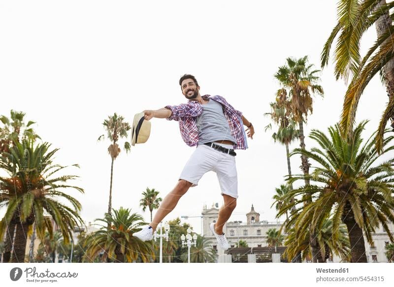 Spain, Barcelona, happy man jumping mid-air surrounded by palm trees men males portrait portraits Leaping Fun having fun funny happiness Adults grown-ups