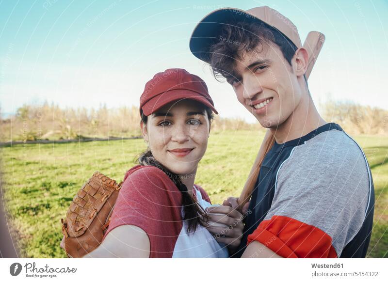 Portrait of smiling young couple with baseball equipment in park Selfie Selfies twosomes partnership couples baseball player baseball players smile people