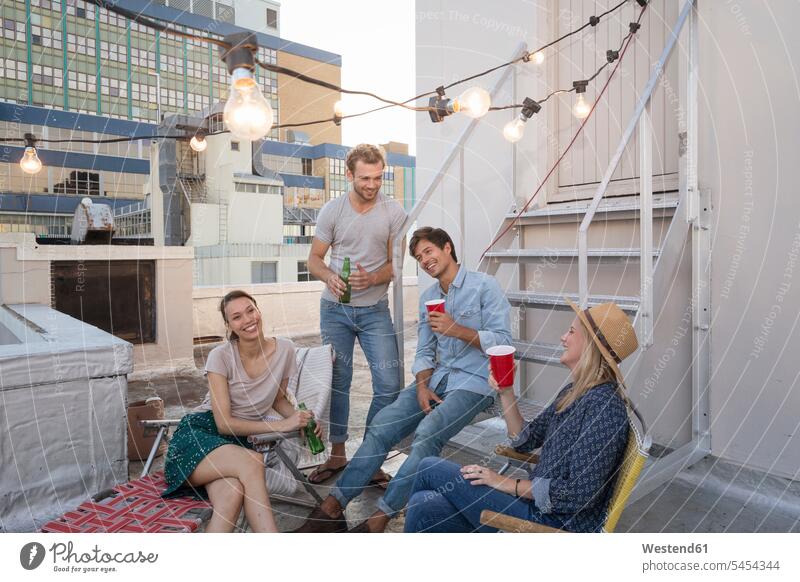 Friends having a rooftop party on a beautiful summer evening enjoying indulgence enjoyment savoring indulging drinking together roof terrace deck summer time