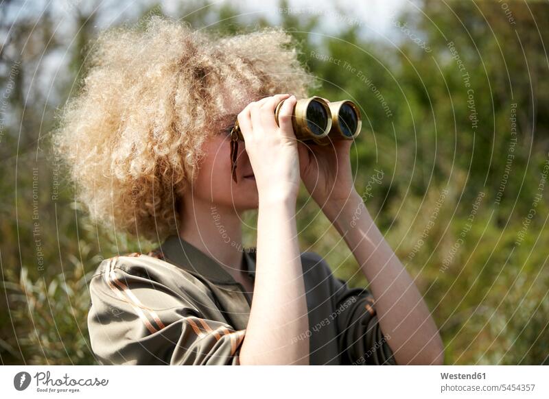Young woman with curly hair looking through old binoculars watching observing observe females women Adults grown-ups grownups adult people persons human being