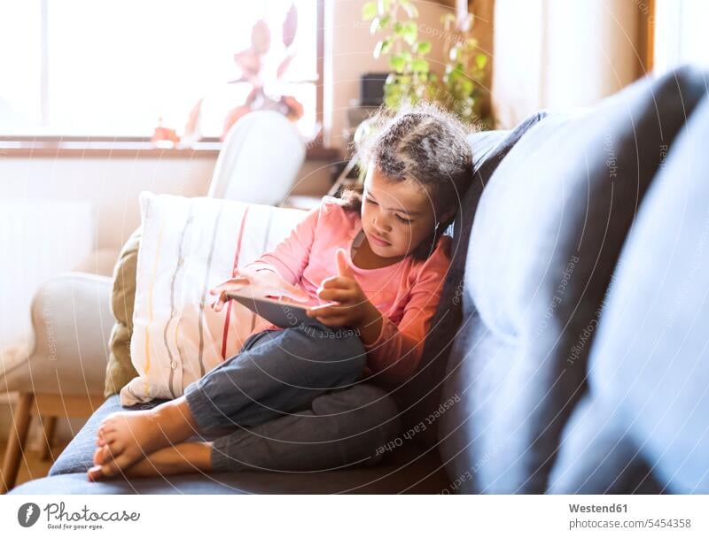 Little girl using sitting tablet, sitting on couch settee sofa sofas couches settees females girls alone solitary solo home at home digitizer Tablet Computer