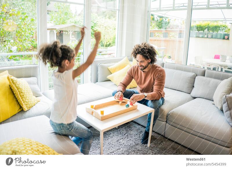 Father and daughter sitting on couch playing foosball settee sofa sofas couches settees Seated wooden toy wooden toys childhood togetherness carefree Ambition