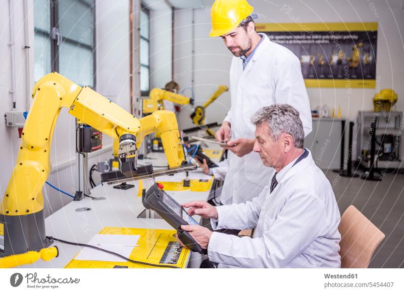 Two engineers in factory looking at device man men males Robot colleagues factories Adults grown-ups grownups adult people persons human being humans