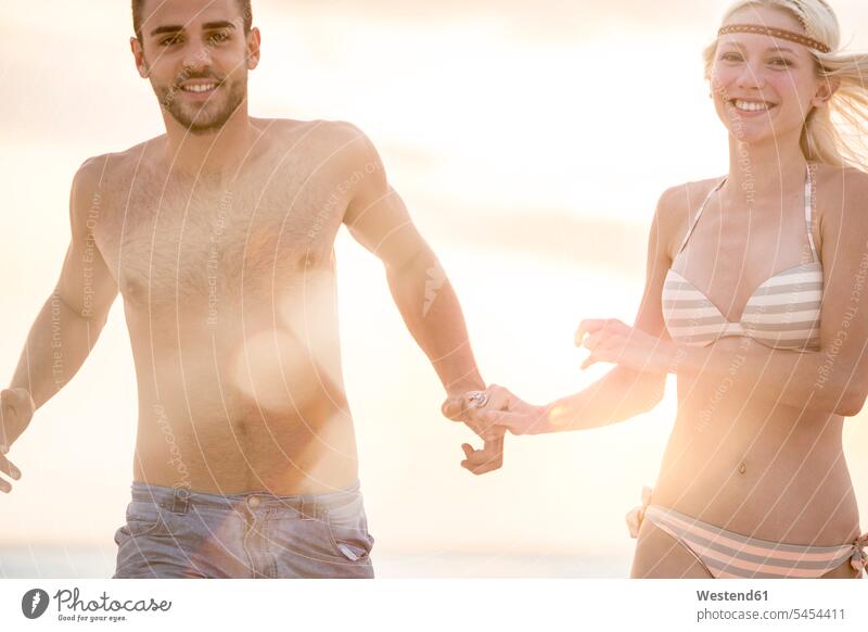 Young couple running on the beach, holding hands vacation Holidays beaches Sea ocean happiness happy in love romantic lyrical Romance Travel water sunshine