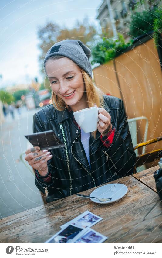 Young tattooed woman sitting in a pavement cafe looking at photos outdoor cafes portrait portraits females women Adults grown-ups grownups adult people persons