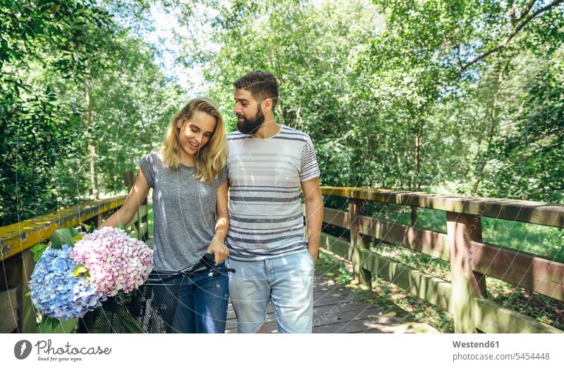 Couple walking on a wooden walkway with a bouquet of hydrangeas in the bicycle basket going couple twosomes partnership couples bikes bicycles path trail paths