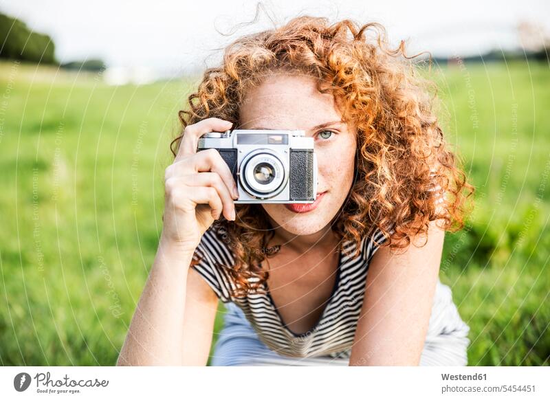 Young woman on a meadow taking picture of viewer with camera photographing portrait portraits females women Adults grown-ups grownups adult people persons
