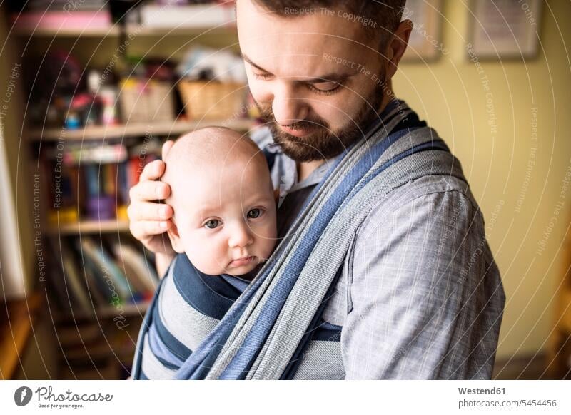 Father with baby son in sling at home carrying father pa fathers daddy dads papa infants nurselings babies parents family families people persons human being