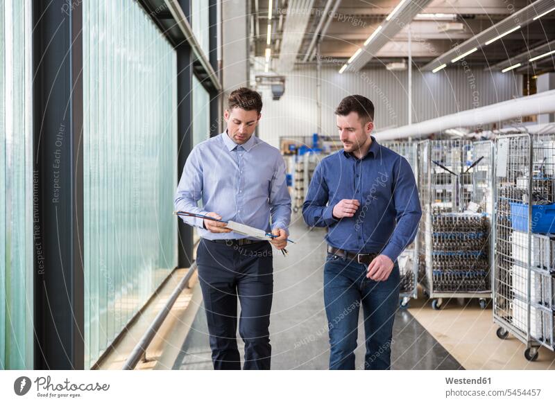 Two men walking in factory shop floor talking about product factories working At Work colleagues man males Adults grown-ups grownups adult people persons