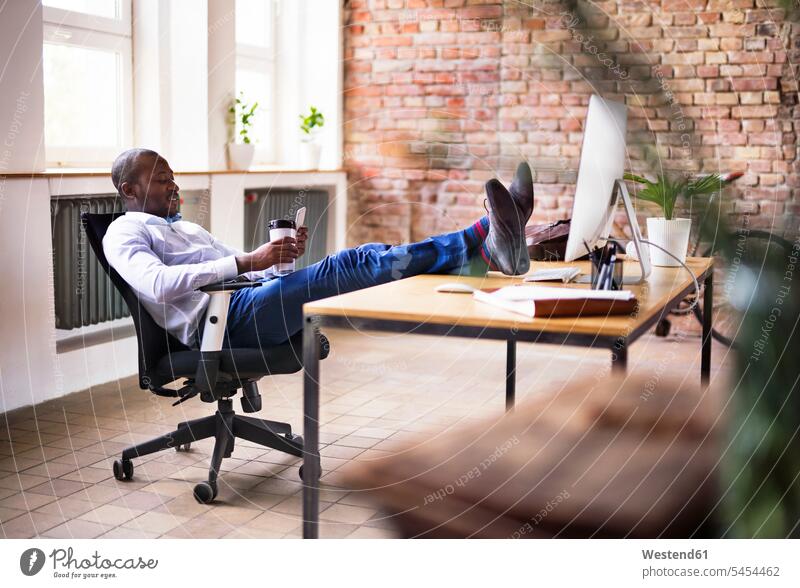 Businessman sitting in office with feet on desk checking cell phone Seated mobile phone mobiles mobile phones Cellphone cell phones offices office room