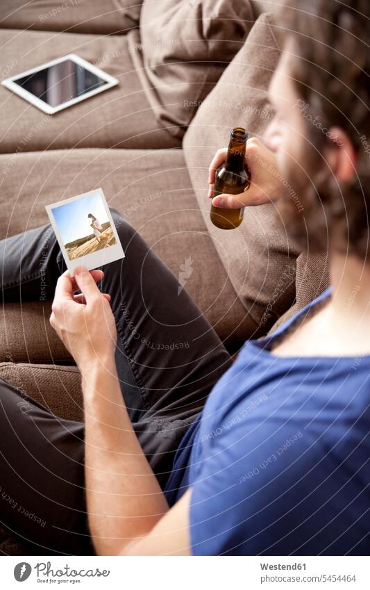 Man sitting on couch with beer bottle looking at instant photo photograph photographs photos man men males image images picture pictures Adults grown-ups