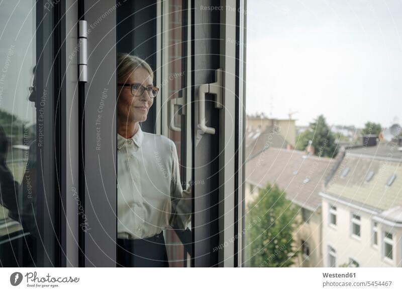 Businesswoman in office looking out of window businesswoman businesswomen business woman business women standing business people businesspeople business world