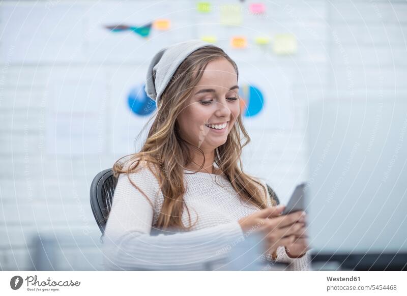Young woman working in office, reading text messages desk desks sitting Seated At Work office worker happiness happy text messaging SMS Text Message young women