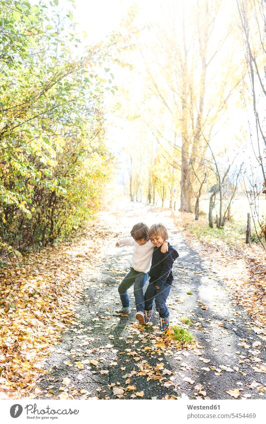 Two little boys playing on autumnal country road friends males brother brothers friendship child children kid kids people persons human being humans