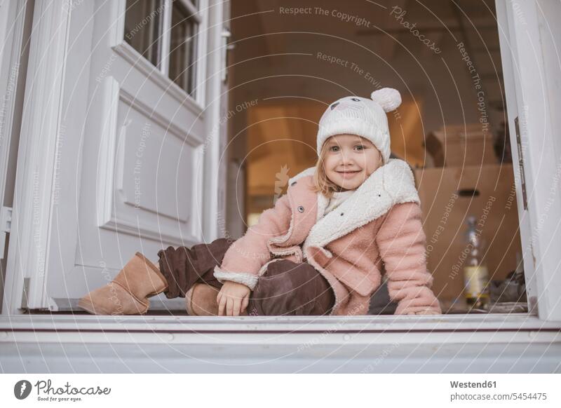 Young girl sitting in entrance, cardboard box moving house move Moving Home females girls Coat Coats cardboard boxes packing case packing cases Seated smiling