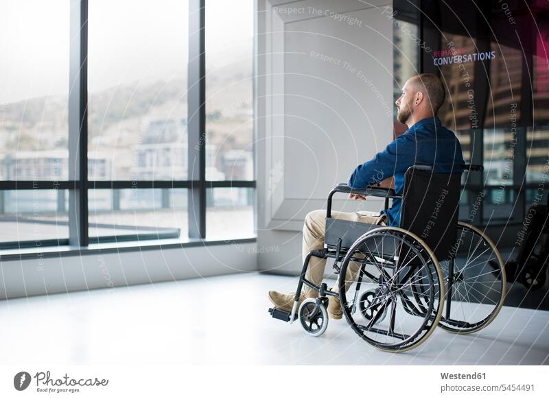 Man in wheelchair looking out of window in office Looking Through Window Looking Through A Window looking through glass handicapped serious earnest Seriousness
