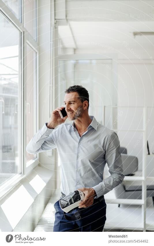 Businessman on cell phone at the window holding VR glasses mobile phone mobiles mobile phones Cellphone cell phones office offices office room office rooms