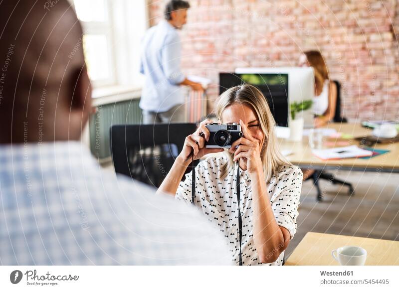 Businesswoman with camera taking picture of colleague in office cameras offices office room office rooms photographing colleagues businesswoman businesswomen