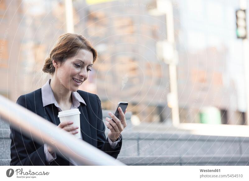 Smiling businesswoman holding cell phone and takeaway coffee businesswomen business woman business women business people businesspeople business world