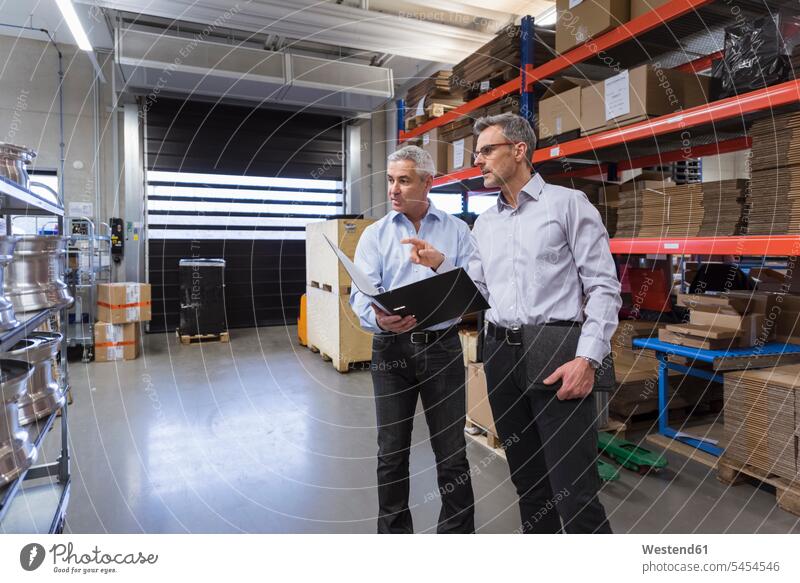 Two businessmen in factory hall talking speaking working At Work colleagues man males storehouse storage warehouse scrutiny scrutinizing Adults grown-ups
