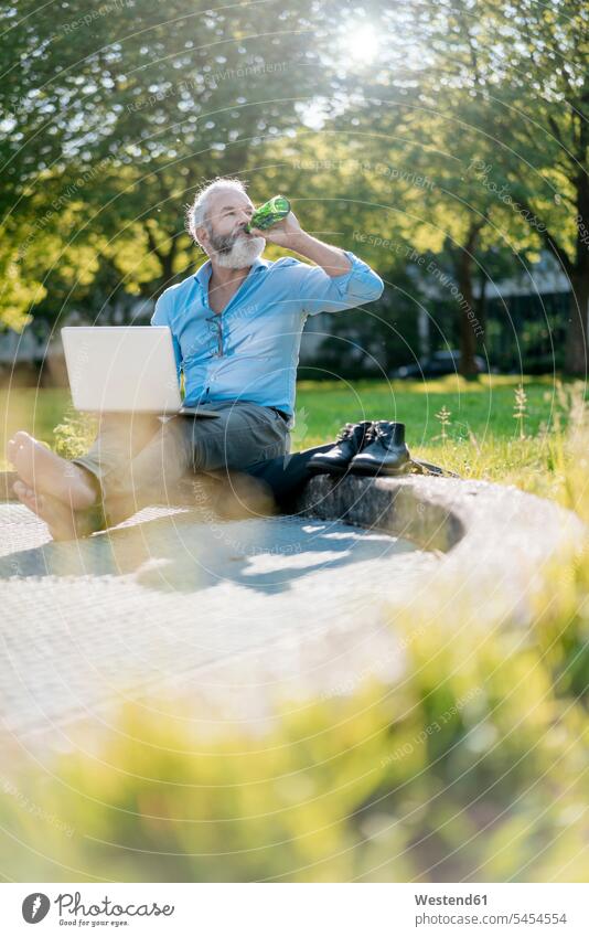 Mature man drinking beer and using laptop in park meadow meadows sitting Seated Laptop Computers laptops notebook men males Beer Beers Ale computer computers