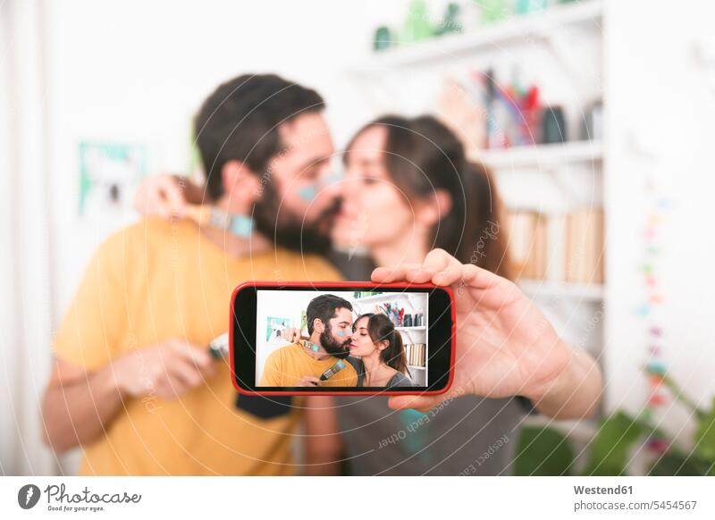 Young couple kissing and taking a selfie with paintbrushes Selfie Selfies mobile phone mobiles mobile phones Cellphone cell phone cell phones kisses twosomes
