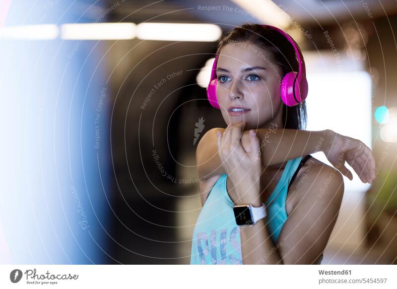 Young woman with pink headphones stretching and listening to music in modern urban setting at night exercising exercise training practising Listening Music
