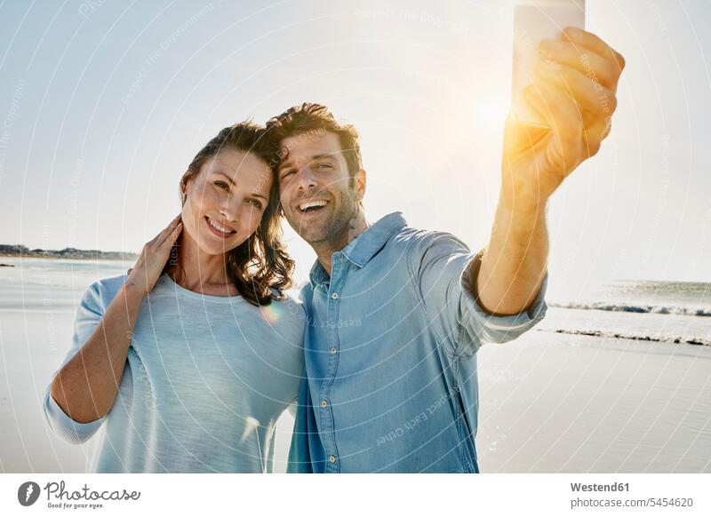 Portrait of happy couple taking selfie on the beach with smartphone beaches Selfie Selfies twosomes partnership couples people persons human being humans