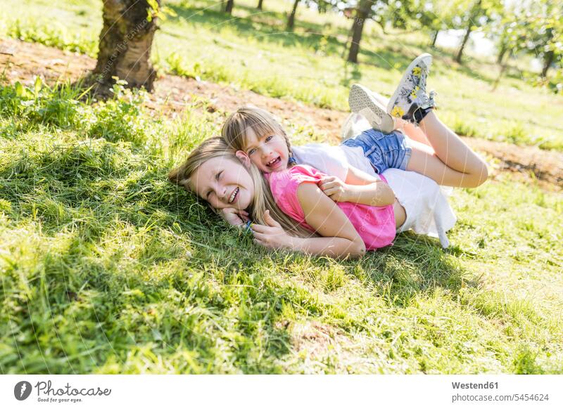 Two happy sisters playing in meadow meadows happiness lying laying down lie lying down garden gardens domestic garden girl females girls siblings