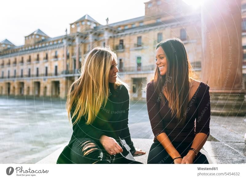 Two smiling young women talking on urban square female friends woman females smile mate friendship Adults grown-ups grownups adult people persons human being