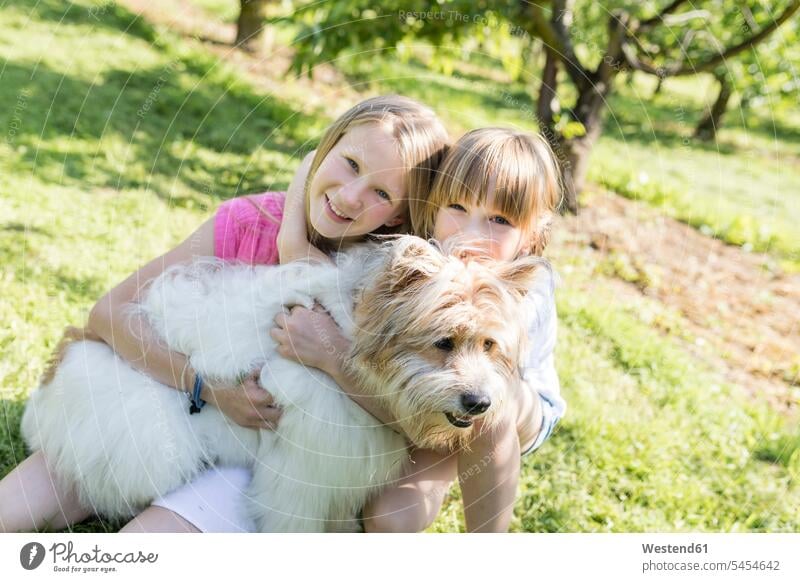 Two smiling sisters cuddling with dog on meadow meadows girl females girls dogs Canine garden gardens domestic garden happiness happy smile child children kid