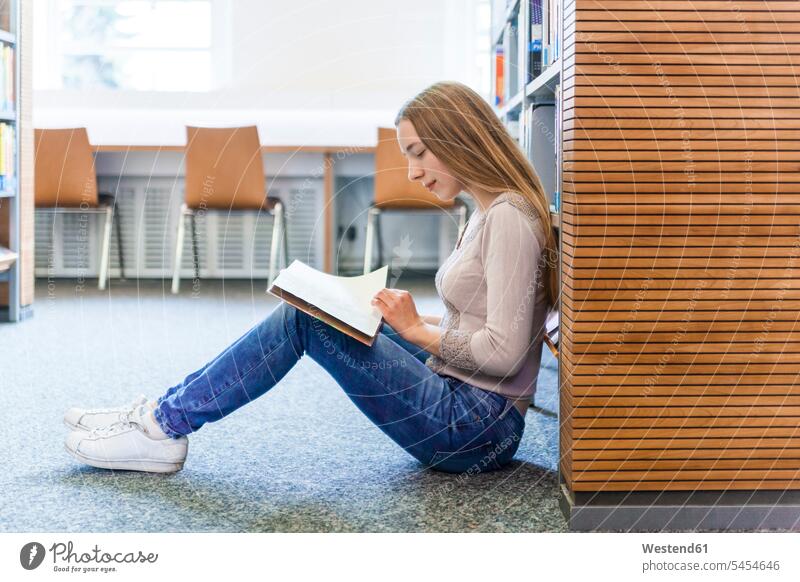 Teenage girl sitting on the floor in a public library reading book books Teenage Girls female teenagers Floor Floors Seated Teenager Teens people persons