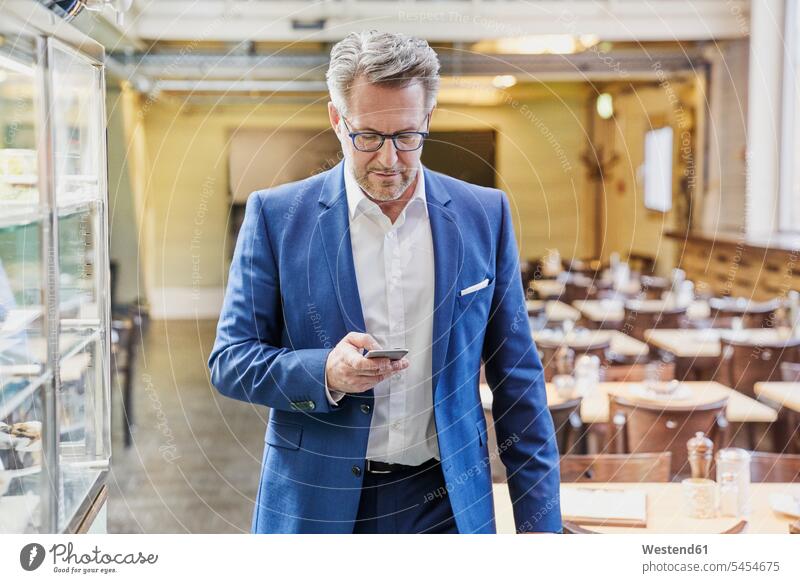 Mature businessman in cafe looking on cell phone Businessman Business man Businessmen Business men mobile phone mobiles mobile phones Cellphone cell phones