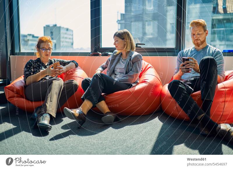Colleagues with cell phones sitting in bean bags in office lounge mobile phone mobiles mobile phones Cellphone offices office room office rooms colleagues