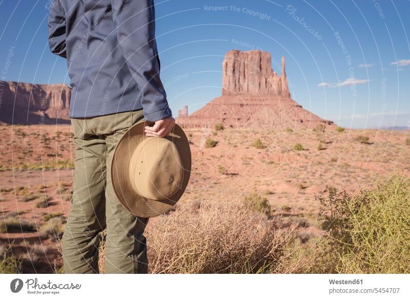 USA, Utah, Young man looking at Monument Valley tourist tourists fascinated fascination mesmerized Adventure adventurous Adventures standing holding hat hats