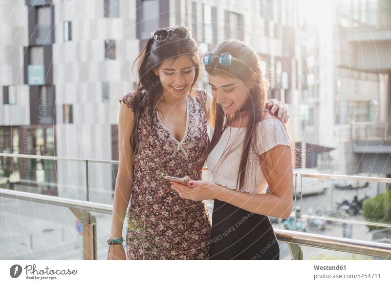 Two smiling young women looking at cell phone in the city mobile phone mobiles mobile phones Cellphone cell phones smile female friends telephones communication