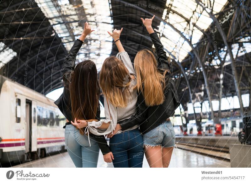 Back view of three young women standing arm in arm on platform Railroad Platform female friends train station transportation mate friendship station building