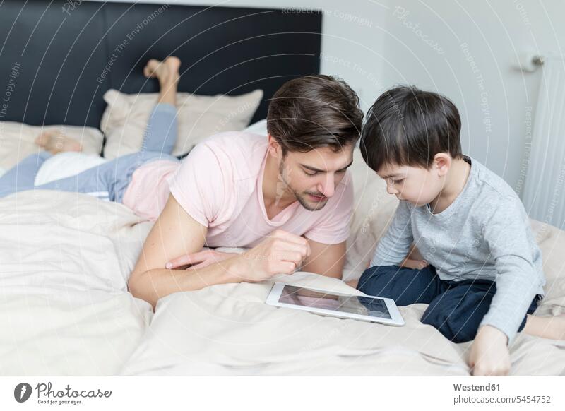 Father and son looking at tablet in bed beds sons manchild manchildren digitizer Tablet Computer Tablet PC Tablet Computers iPad Digital Tablet digital tablets