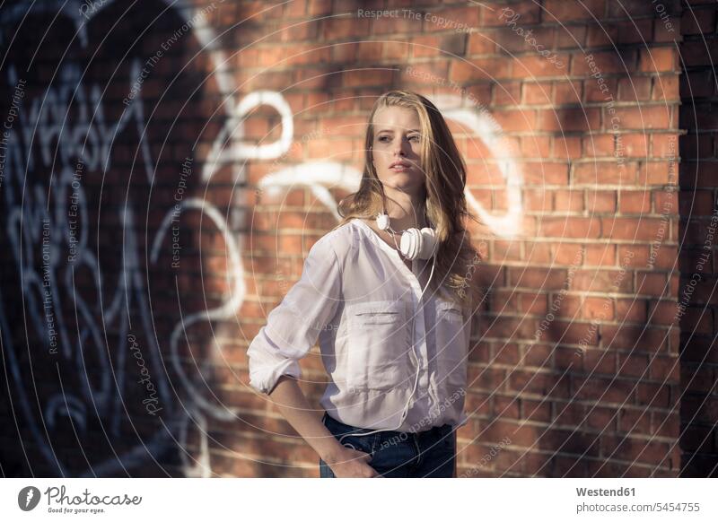 Portrait of young woman with headphones in front of brick wall portrait portraits females women Adults grown-ups grownups adult people persons human being