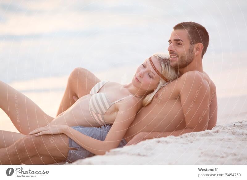 Young couple sitting on the beach, embracing eroticism sexuality in love romantic lyrical Romance beaches vacation Holidays Sea ocean Travel water bikini