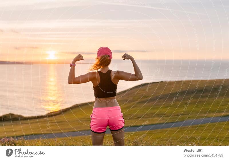 Young woman looking at the sea after workout, flexing muscles exercising exercise training practising females women Adults grown-ups grownups adult people