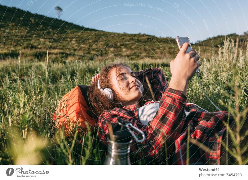 Teenage girl with backpack lying on a meadow listening music with headphones and cell phone laying down lie lying down Teenage Girls female teenagers headset