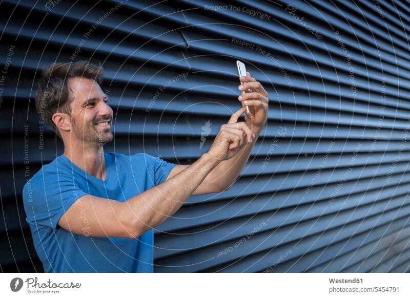 Man standing in front of roller shutter, taking a selfie mobile phone mobiles mobile phones Cellphone cell phone cell phones confidence confident Smartphone