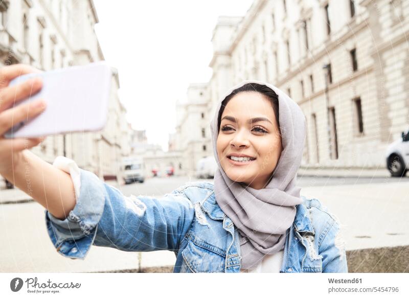 UK, England, London, young woman wearing hijab taking a selfie in the city headscarf head scarf head scarves Head Scarf head cloths headscarves Muslim